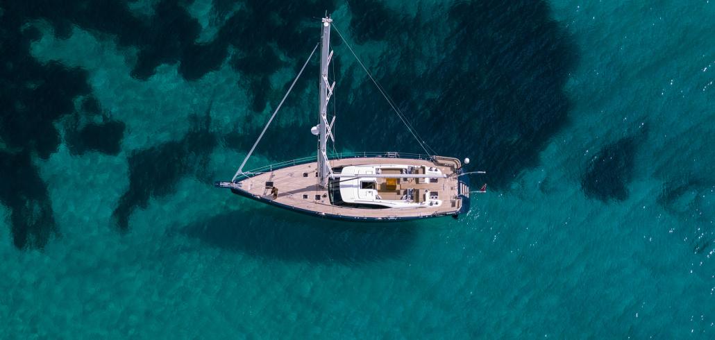 Oyster yacht at anchor over crystal water from above
