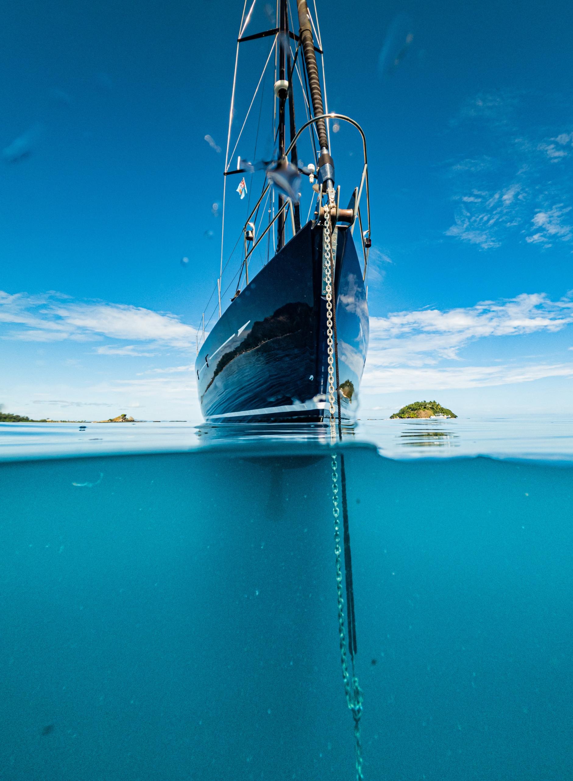 Yacht bow and polished anchor chain in clear blue water